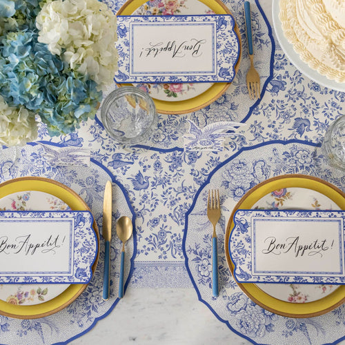 Place settings on a table with flowers, blue and white placemats and table runner.
