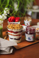 Jar of yogurt parfait with granola on a wooden tray with an Oregon Growers jar of blueberries in the background.