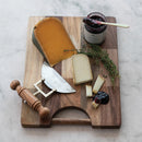 A jar of blueberry lemon thyme jam on a wooden cutting board with cheeses, thyme, and a cheese cutter, all on a marble surface.
