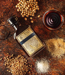 Bottle of Blue Grass Solstice Soy Sauce with soybeans, wheat grains, and salt on a rustic surface
