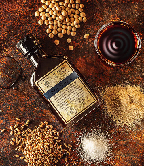 Bottle of Blue Grass Solstice Soy Sauce with soybeans, wheat grains, and salt on a rustic surface
