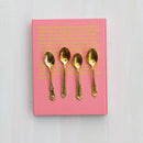 Pink book with gold text and four brass spoons on a white background