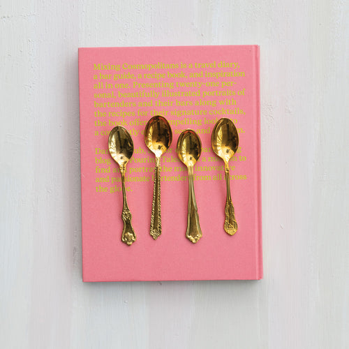 Pink book with gold text and four brass spoons on a white background