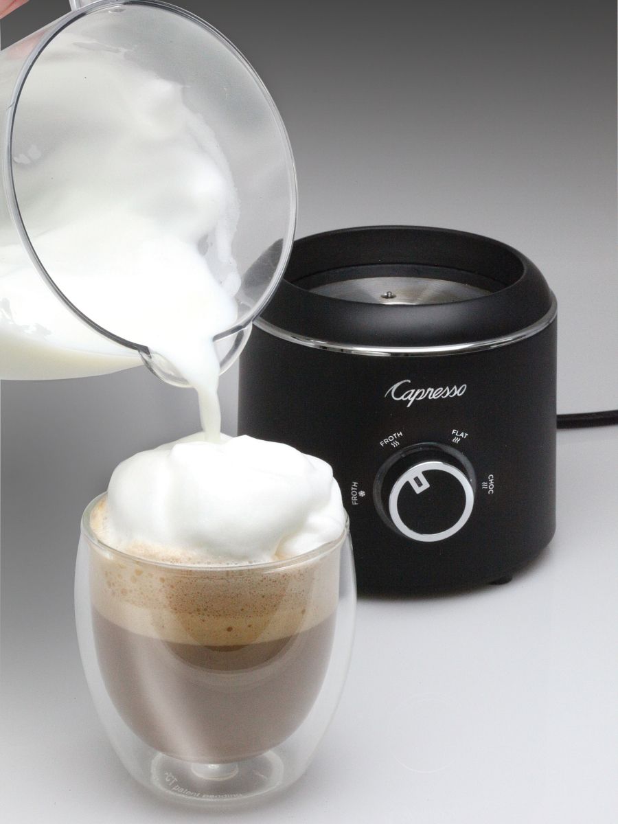 Capresso milk frother with a glass of coffee and milk being poured into it on a white background.