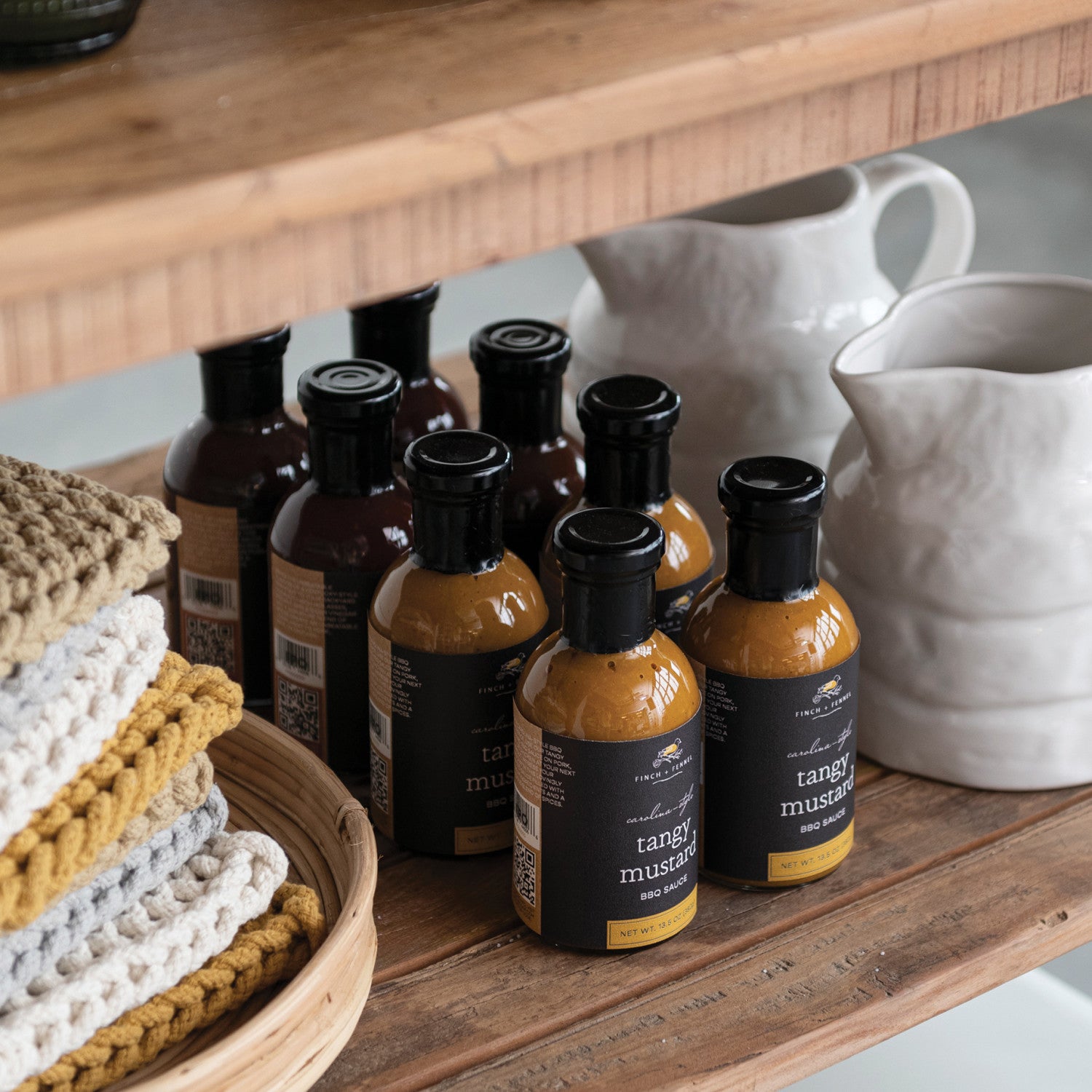 Bottles of tangy mustard on a wooden surface with kitchen items in the background