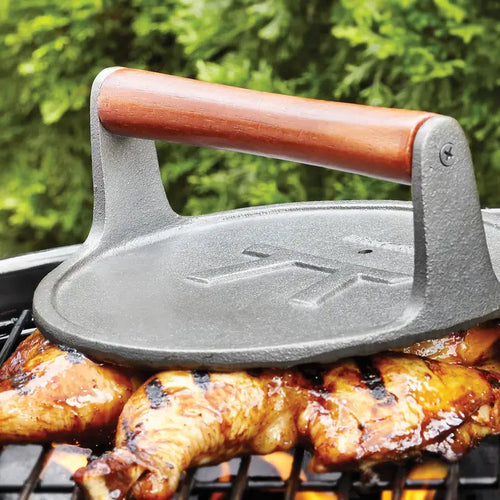 Cast iron griddle on a grill with chicken being cooked