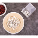 Pie crust with white pie weights on a gray surface, next to a bowl of red berries and a container of additional pie weights.
