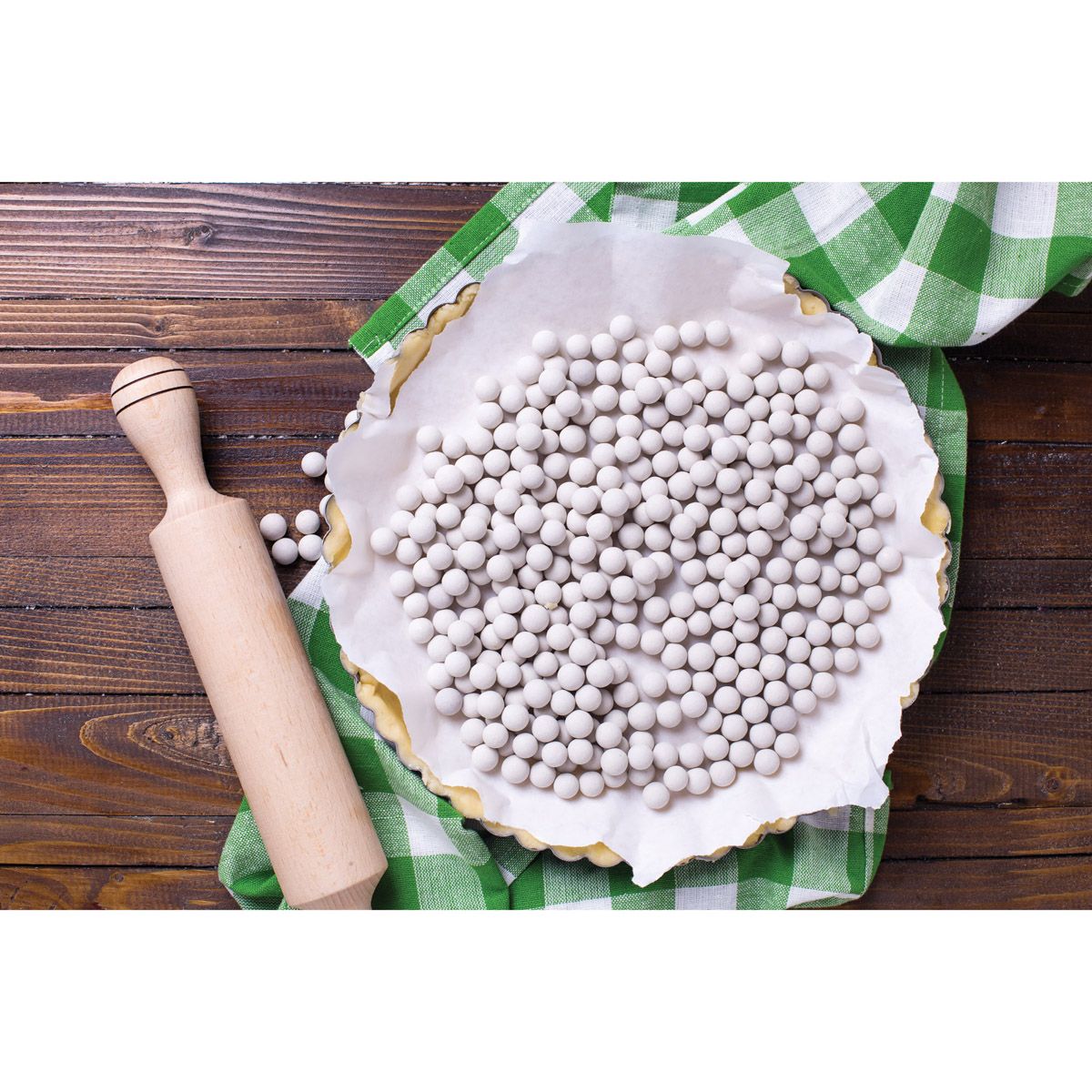 Pie with white paper and pie weights on a wooden table with a rolling pin.