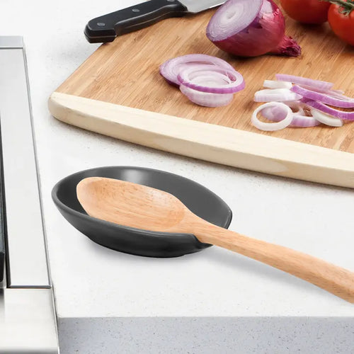 Black spoon rest with wooden spoon on a kitchen counter with cutting board and sliced onions in the background