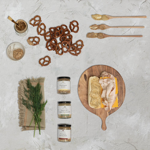 Assorted food items including pretzels, bread with cheese, and jars on a textured surface.
