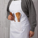 A person wearing a white cotton apron with wooden utensils in the pockets.