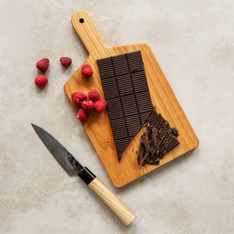 Chocolate bars on a wooden cutting board with raspberries and a knife on a light surface