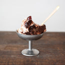 Metallic dessert bowl with ice cream and a wooden spoon on a wooden surface