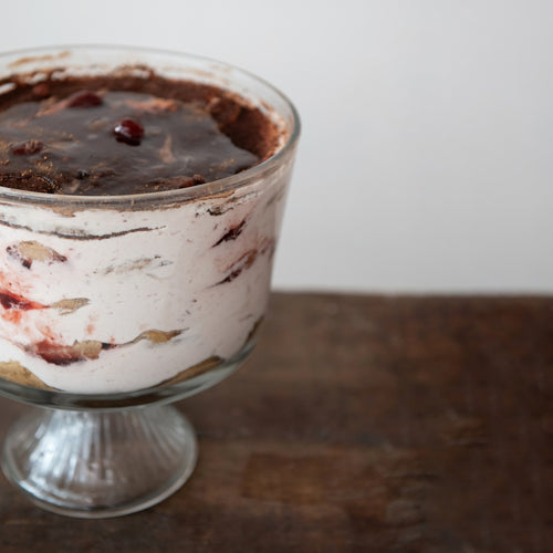Dessert in a glass bowl with layers of cream and chocolate on a wooden surface.