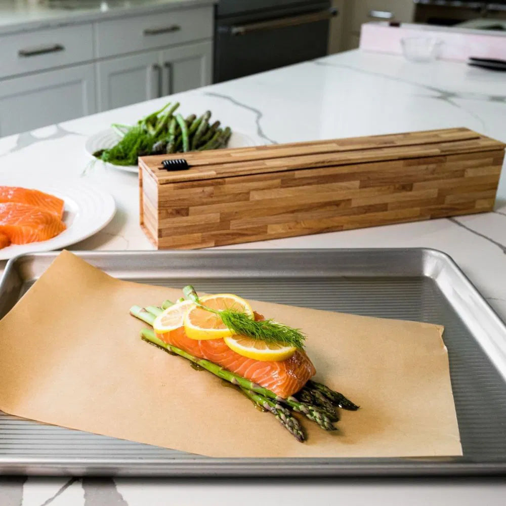 Parchment paper dispenser on a kitchen counter with salmon and asparagus on a sheet of paper.