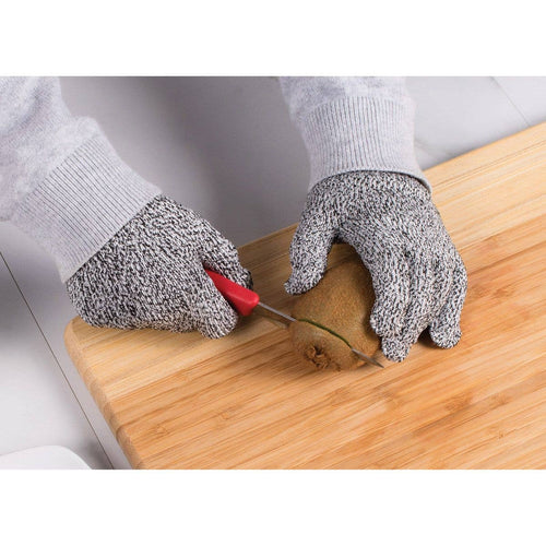 Person cutting a kiwi with a knife on a wooden cutting board, wearing protective gloves.