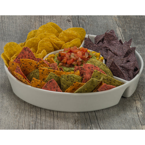 Assorted colorful tortilla chips in a white bowl with guacamole and salsa on a wooden surface.
