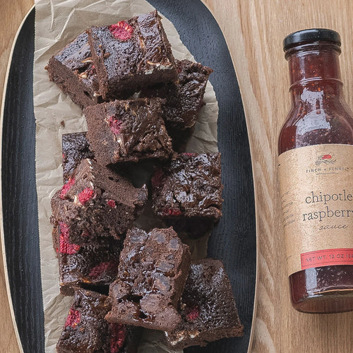 Chocolate brownies with raspberry pieces on a plate next to a bottle of chipotle raspberry sauce.