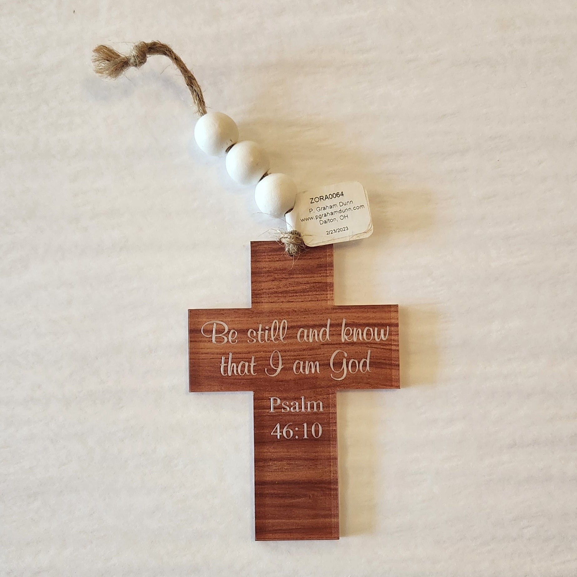Wooden cross with engraved text and white beads on a beige background