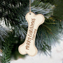 A wooden customizable Christmas ornament in the shape of a dog bone hanging from a fir tree.