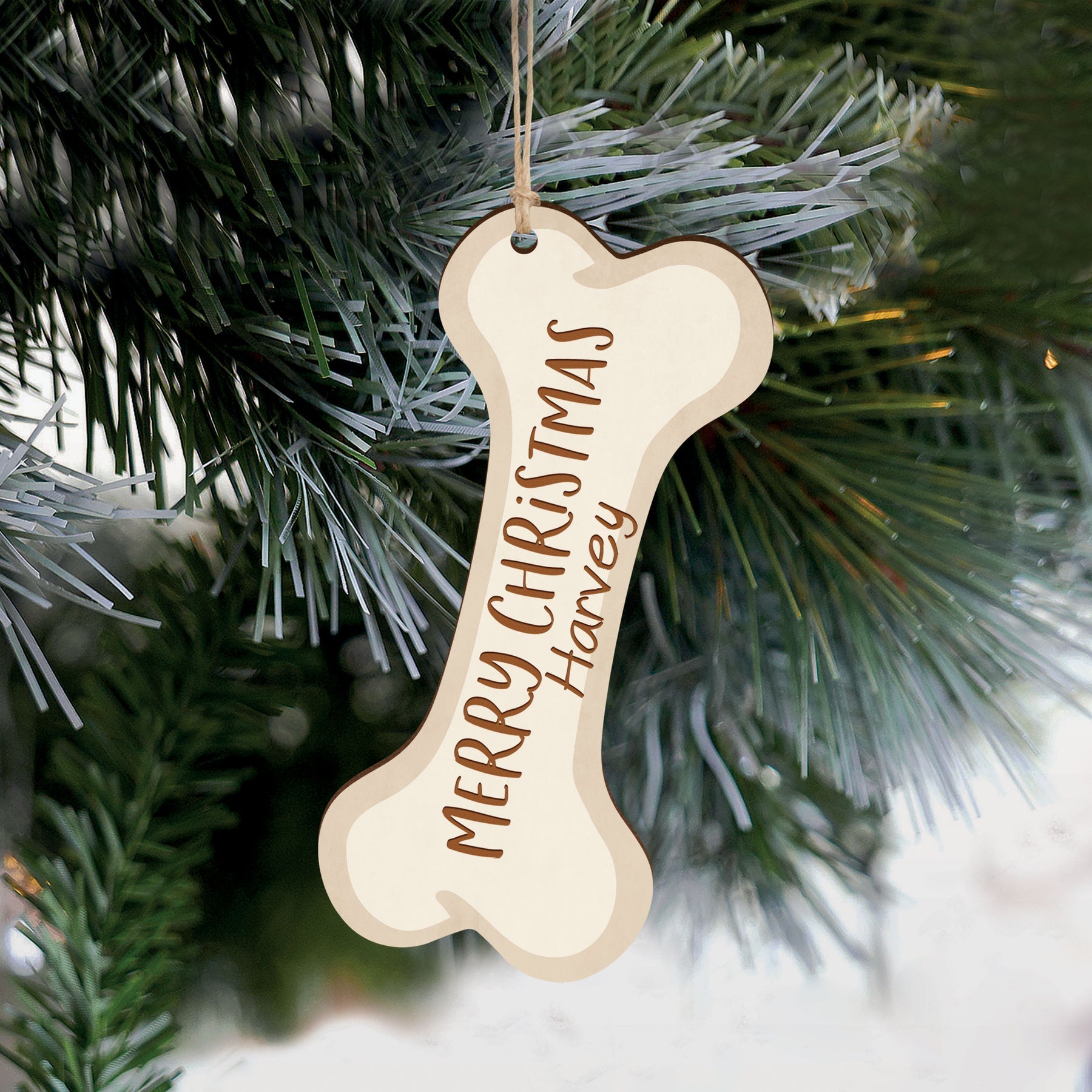 A wooden customizable Christmas ornament in the shape of a dog bone hanging from a fir tree.