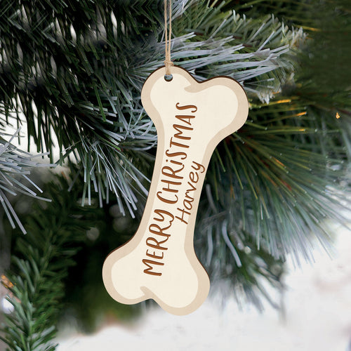 A wooden customizable Christmas ornament in the shape of a dog bone hanging from a fir tree.