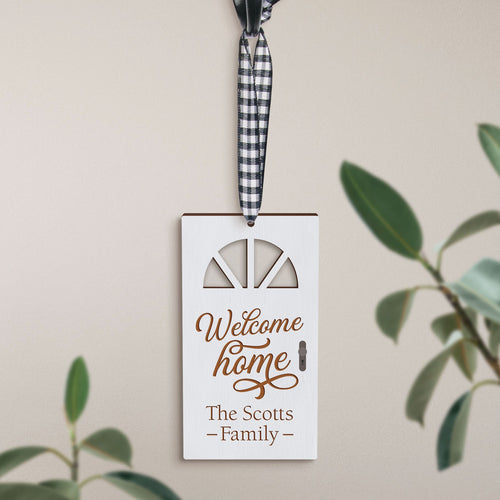 A customizable white Christmas ornament hanging by a ribbon. It has text that reads 'Welcome HOME' with a scripted signature-like font, and a space beneath for personalization.