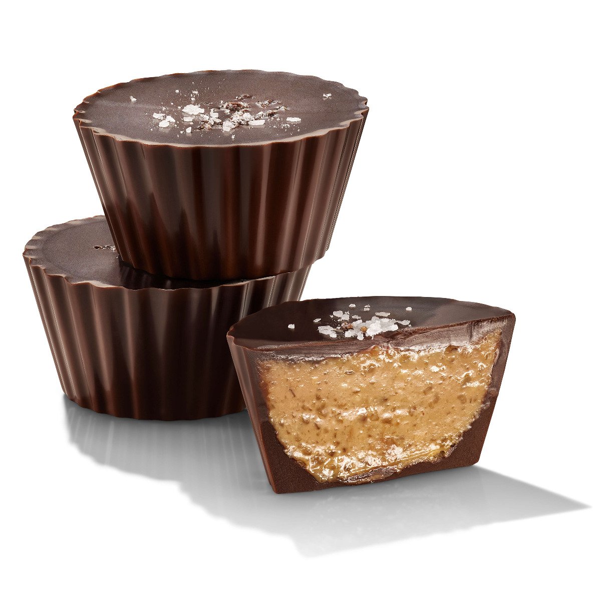Two dark chocolate peanut butter cups with sea salt on top, one whole and one cut in half to show the inside.