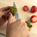 Person cutting a strawberry with a knife on a wooden surface