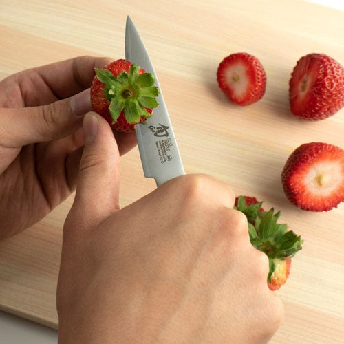 Person cutting a strawberry with a knife on a wooden surface