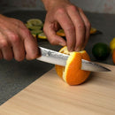 Person cutting an orange with a knife on a wooden cutting board.