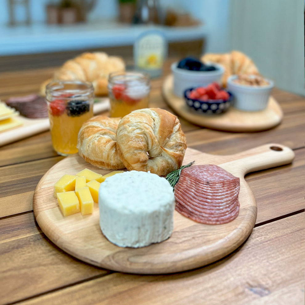 Wooden platter with cheese, salami, and croissants on a wooden table.