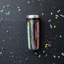 Spice shaker filled with various sprinkles on a dark surface with colorful sprinkles scattered around.