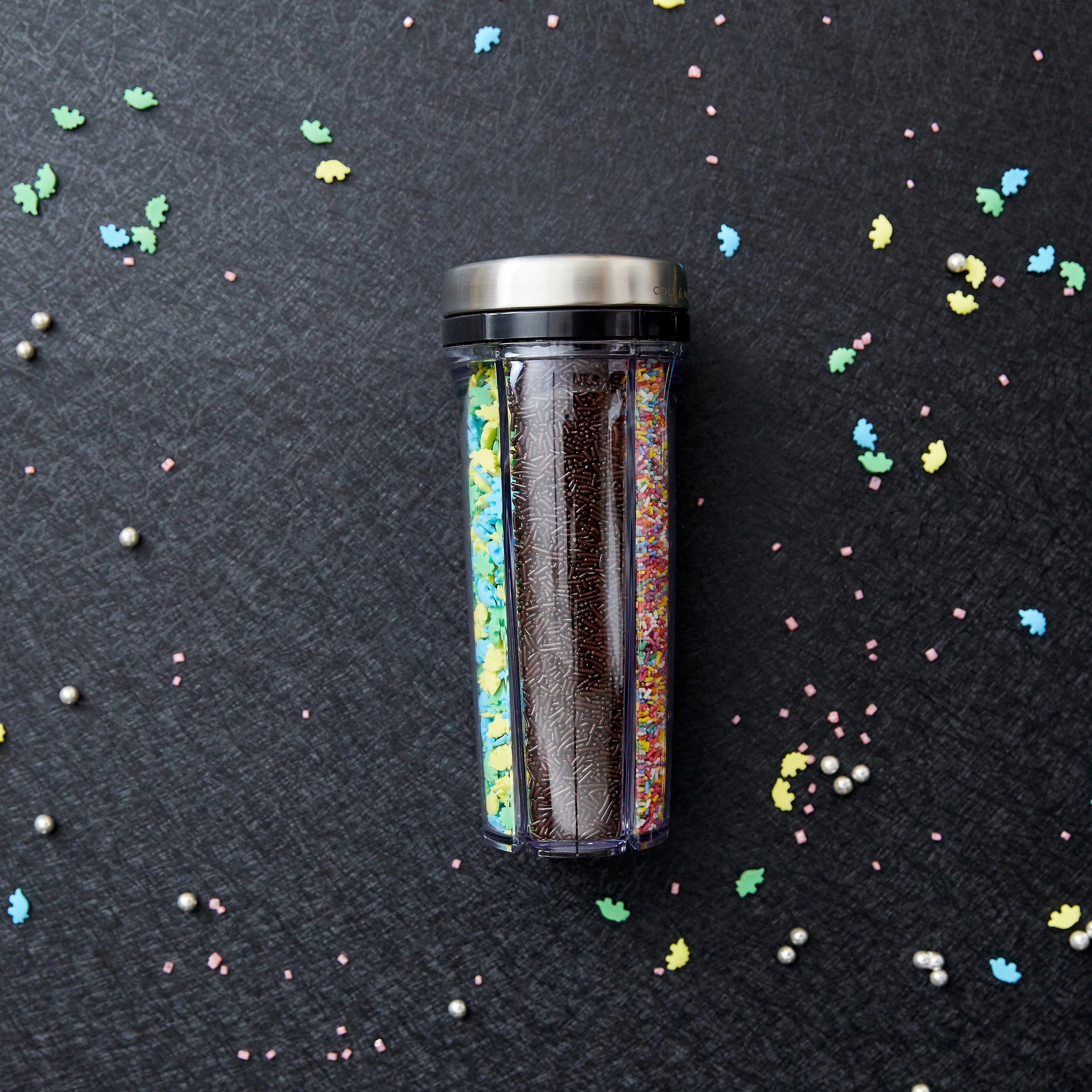 Spice shaker filled with various sprinkles on a dark surface with colorful sprinkles scattered around.