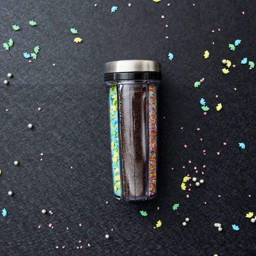 Spice shaker filled with various sprinkles on a dark surface with colorful sprinkles scattered around.