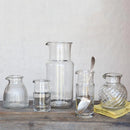 Set of clear glass carafes and other containers on a wooden surface with a neutral background
