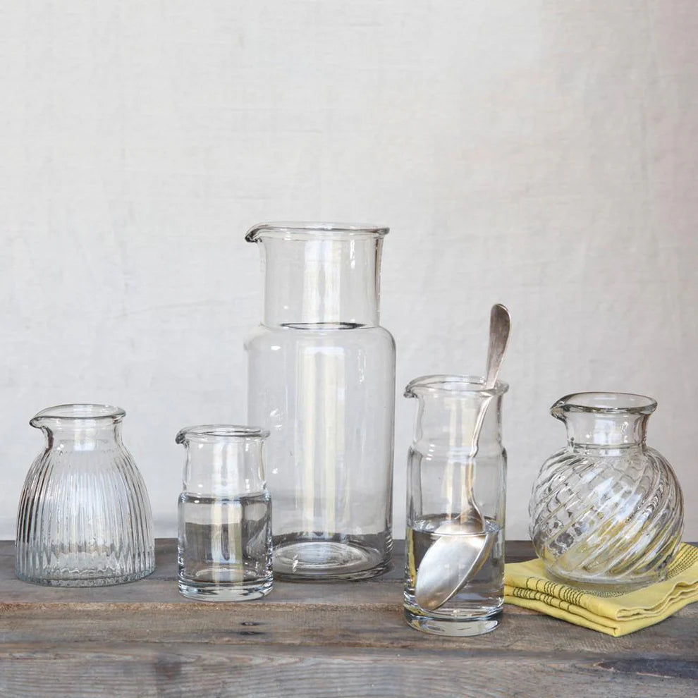 Set of clear glass carafes and other containers on a wooden surface with a neutral background