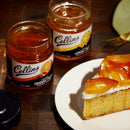 Two jars of Collin's preserves and a slice of cake with candied fruit on a wooden table.