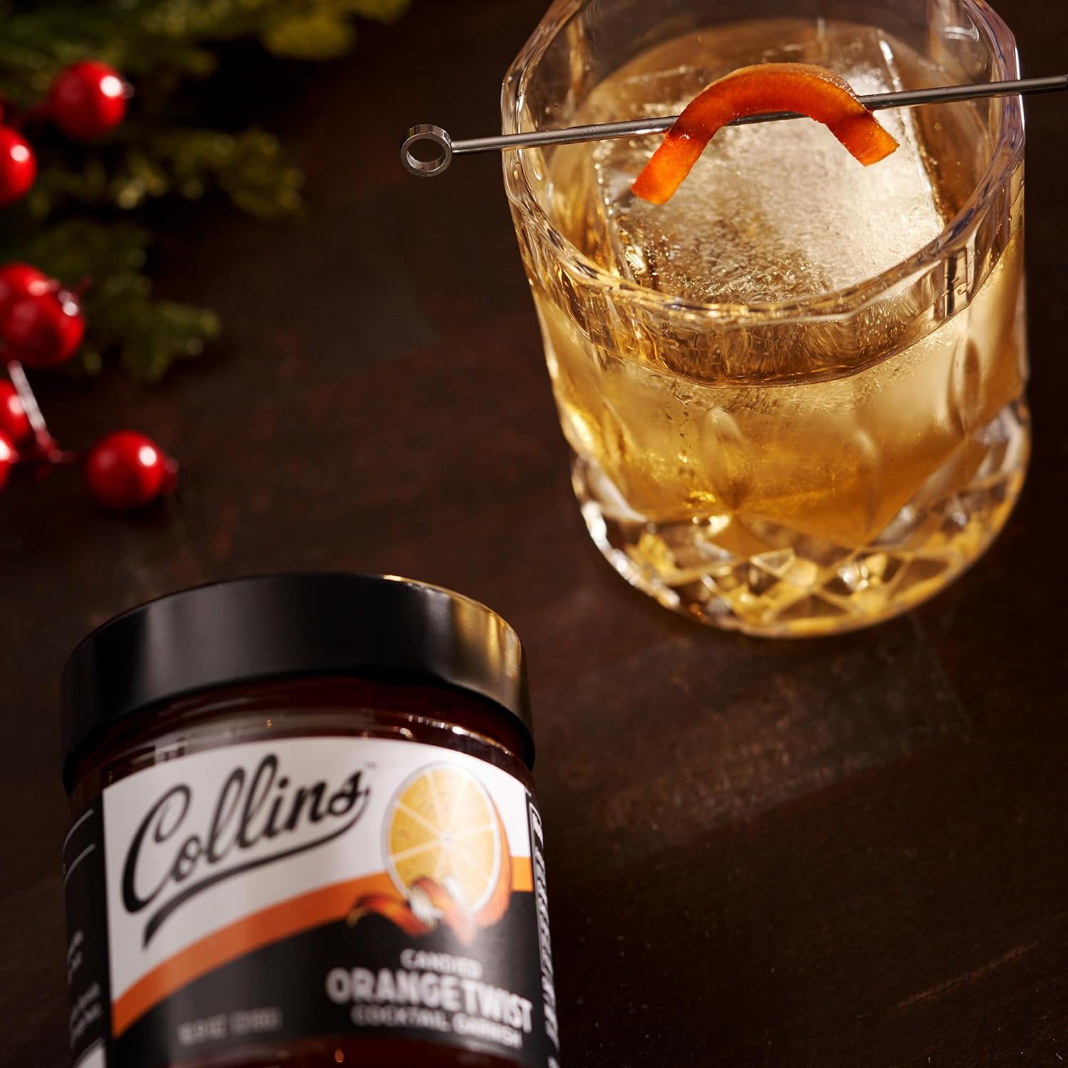 Collins orange twist garnishes jar with a cocktail garnished with an orange peel on a wooden surface.