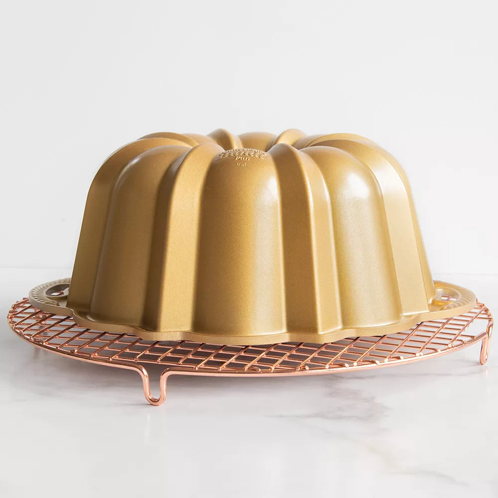 Gold Bundt cake pan on a copper cooling rack against a white background