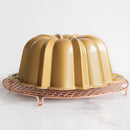 Gold Bundt cake pan on a copper cooling rack against a white background