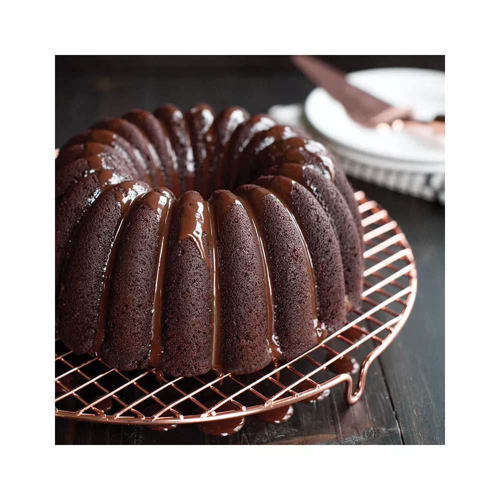 Chocolate bundt cake with a glossy glaze on a copper wire rack.