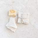 Bar of soap and folded white kitchen dish cloths on a textured white surface