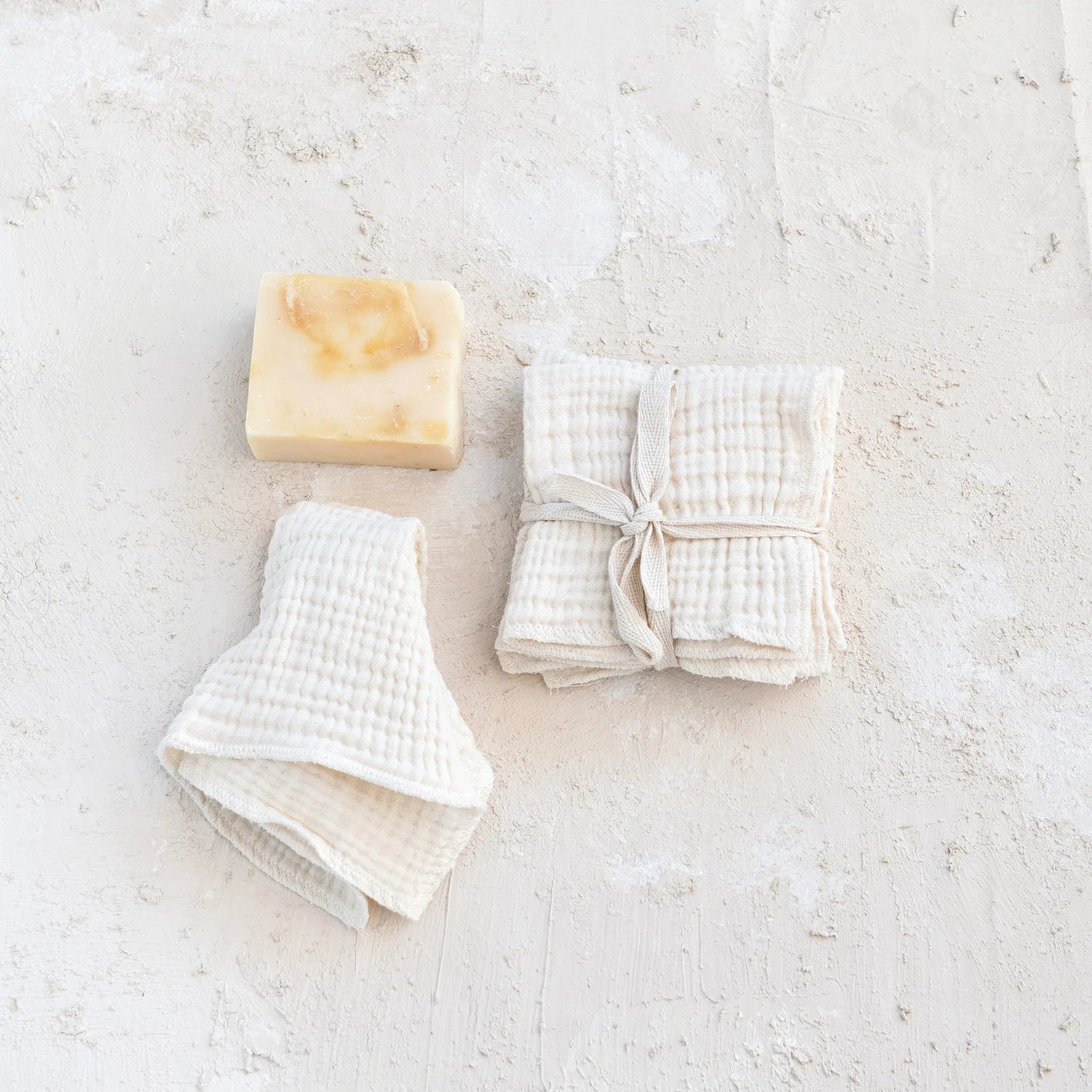 Bar of soap and folded white kitchen dish cloths on a textured white surface