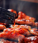 Grilling sausages with a brush applying sauce on a grill