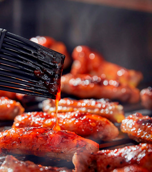 Grilling sausages with a brush applying sauce on a grill