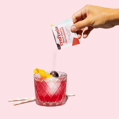 Hand pouring a Craftmix drink mix into a glass with a pink background
