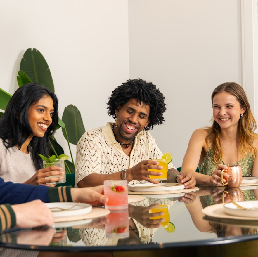 Three people sitting around a table with drinks, smiling and enjoying each other's company.