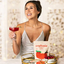 Woman in a silver dress holding a cocktail and a bag of craftmix cranberry vanilla mix.