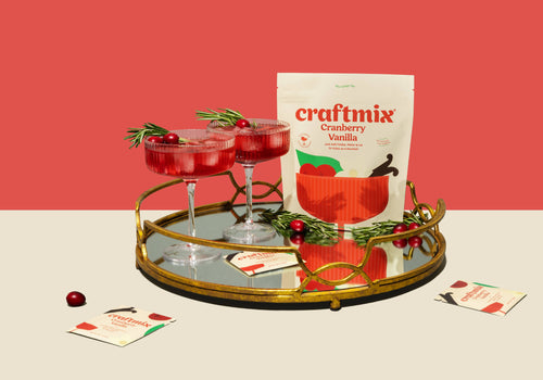 Two red cocktails in glasses with a 'Craftmix Cranberry Vanilla' package on a decorative tray against a red background.